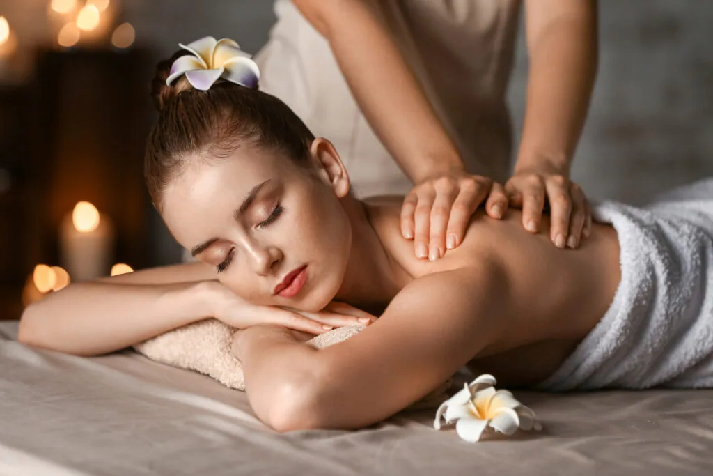 Woman receiving a back massage from a therapist in a spa setting with white flowers and warm lighting