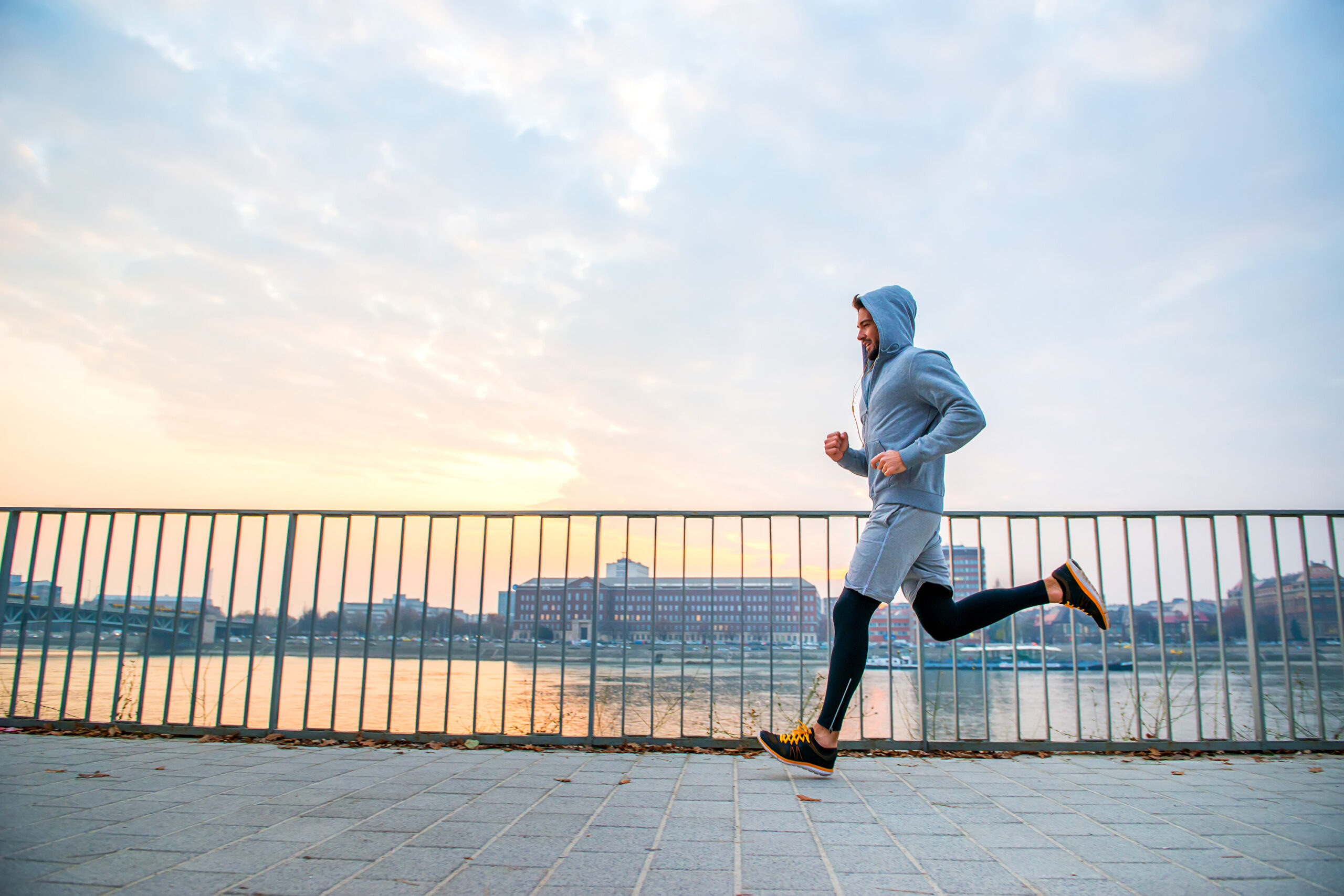 A handsome young man running in the sunset next to a fence on the riverside