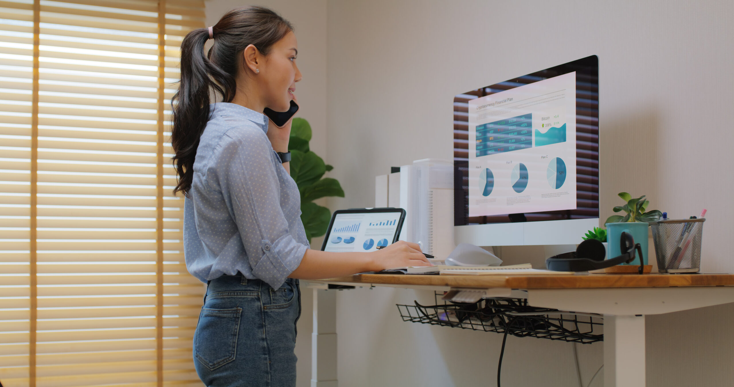 Electric adjustable standing desk in small office workspace for PC desktop computer worker. Asia people young woman relax remote work at home proper height up workstation physical workforce challenge. The Standing Desk Dilema